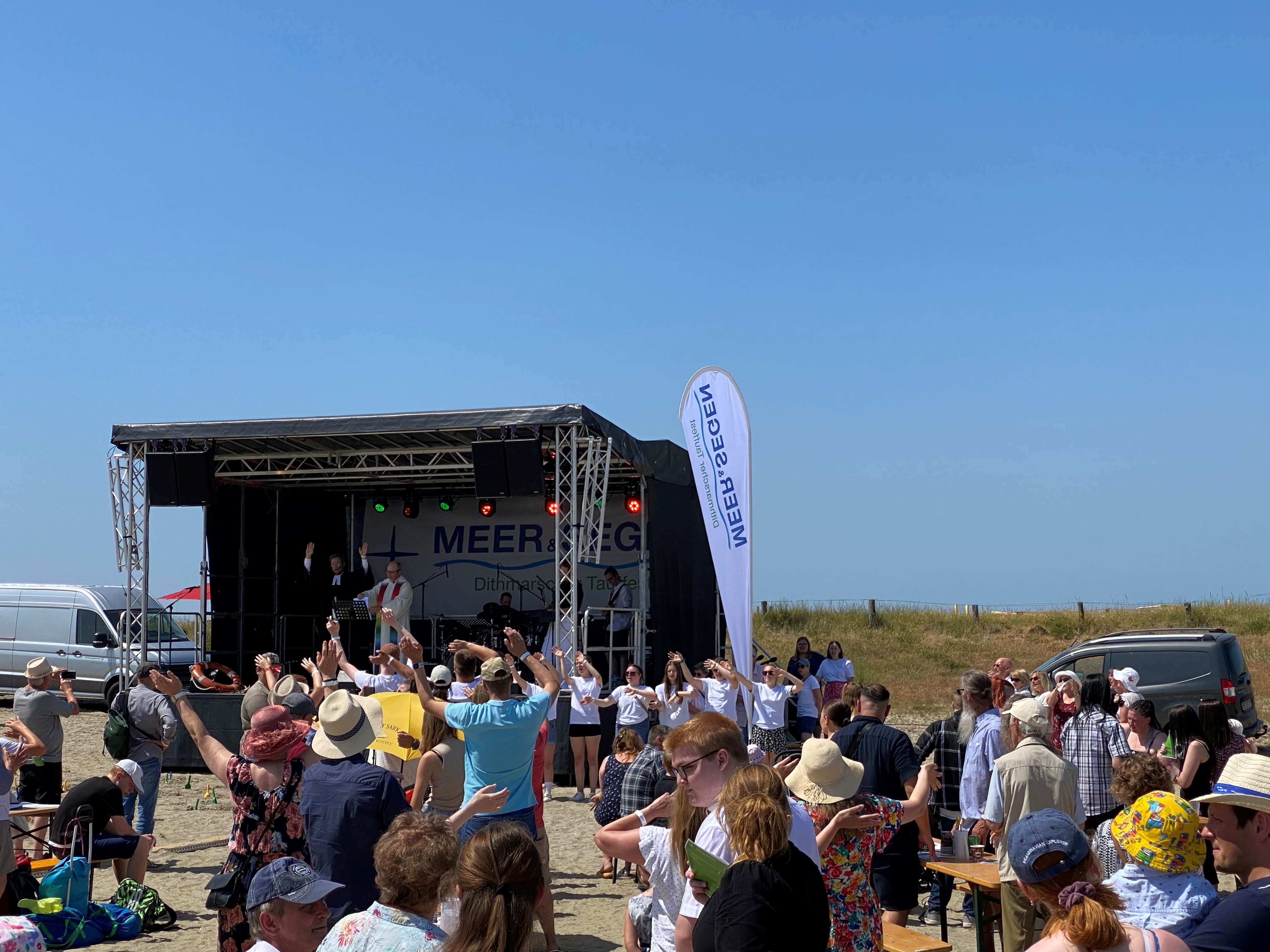 Menschen versammeln sich vor einer Bühne am Strand.