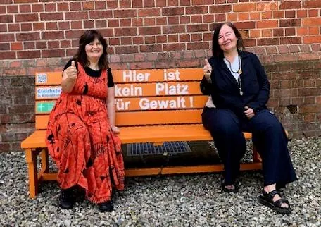 Zwei Frauen auf einer Bank mit "Hier ist kein Platz für Gewalt!" Schild.