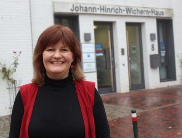 Frau lächelt vor dem Johann-Hinrich-Wichern-Haus.