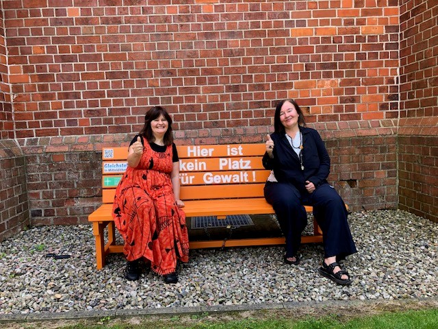 Zwei Frauen auf einer Bank mit "Hier ist kein Platz für Gewalt!" Schild.