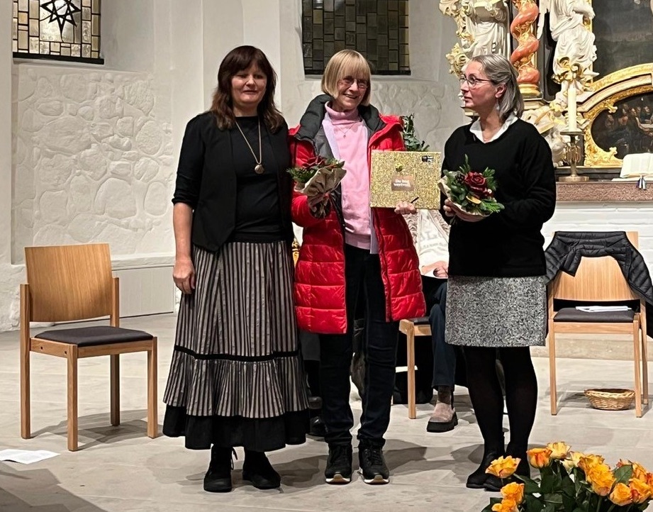 Drei Frauen halten Geschenke in einer Kirche.